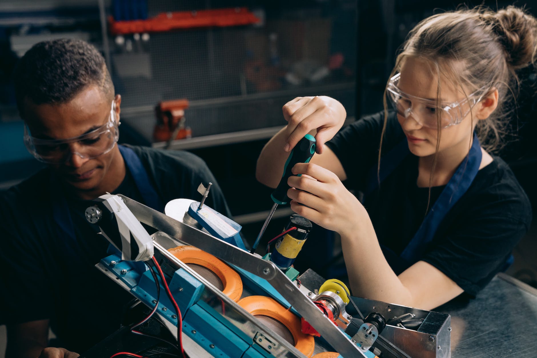 woman in black shirt wearing protective goggles holding black and green screw driver